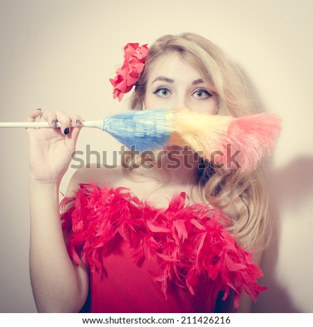 picture of gorgeous funny young blond pinup girl having fun holding dust sweeping brush and looking back at camera on white or light copy space background portrait closeup