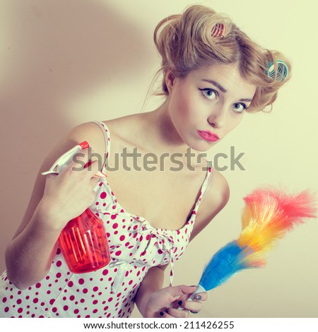 gorgeous funny blond pinup lady having fun holding sprinkler and dust brush in hands looking at camera over white or light copy space background portrait picture