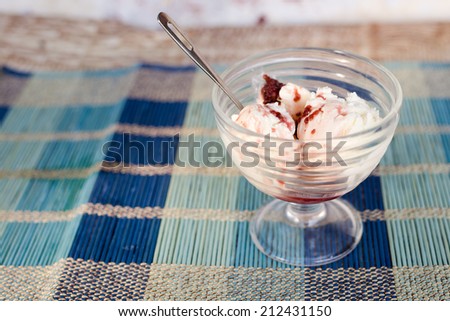 Glass bowl of ice cream with raspberry topping on blue straw napkin