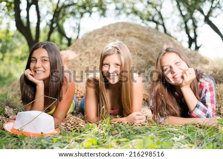 closeup portrait of 3 pretty girls having fun relaxing lying on hay happy smiling with excellent white teeth & looking at camera on green summer outdoors copy space background