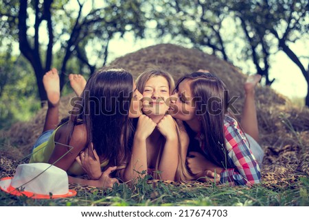 closeup portrait of 3 pretty girls having fun kissing friend relaxing lying on hay happy smiling on green summer outdoors copy space background