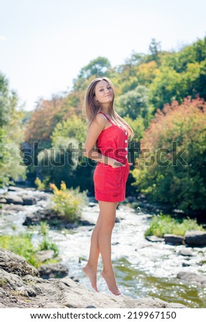 Young woman jumping or flying on cliff edge over fast mountain river on summer or early autumn outdoor copy space background