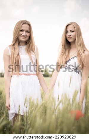 Two young women happy smiling blond girl friends walking in green field & looking at camera on summer outdoors background