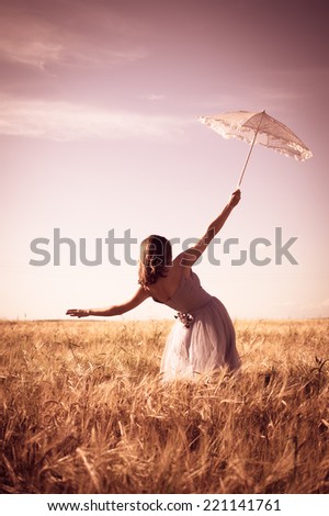 alone in the field: elegant romantic woman in long white dress having fun holding up parasol standing back to camera on blue sky copy space background