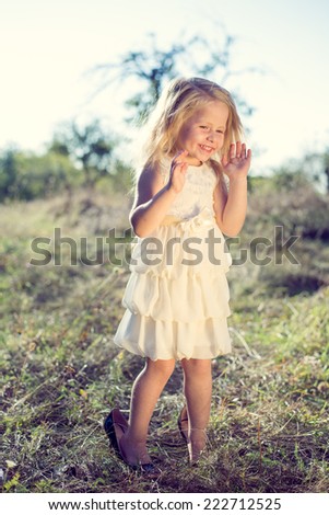 Portrait of happy little girl trying on sisters or moms high heel shoes and smiling on summer green path copy space background