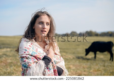 joyful cowgirl: active beautiful young woman in white shirt having fun and smiling among cows looking away on green meadow copy space background