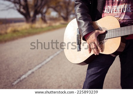 Closeup image of male hand on guitar strings on autumn highway copy space background