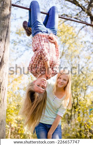 Two teenage girls having fun in park hanging upside down on green countryside rural copy space background