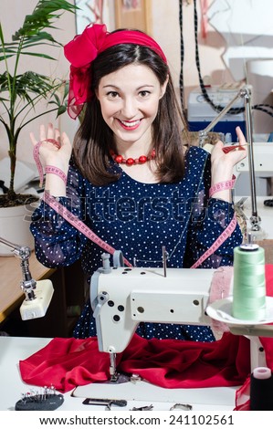 portrait of young pretty woman in polka dot dress with sewing machine and measuring tape happy smiling & looking at camera