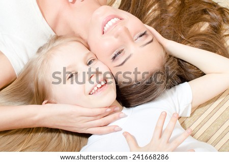 closeup portrait of beautiful attractive woman with child girl lying face to face happy smiling & looking at camera