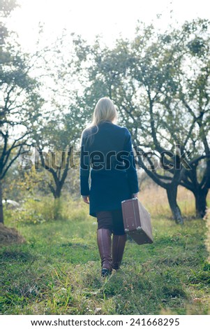 walking away young lady in retro overcoat with vintage suitcase in autumn park copyspace background