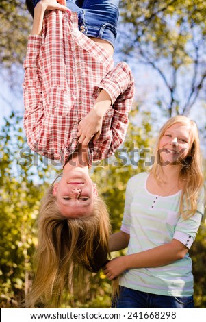 Two teenage girls having fun in park hanging upside down on green countryside rural copy space background