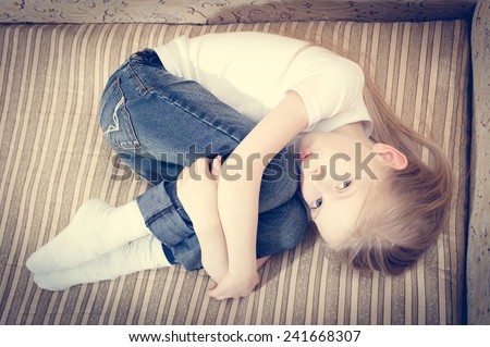 portrait of beautiful child blond girl lying on the sofa hugging knees & looking at camera