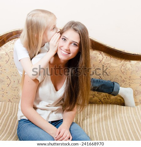 picture of young pretty woman sitting on a couch and the girl child whispers something in her ear