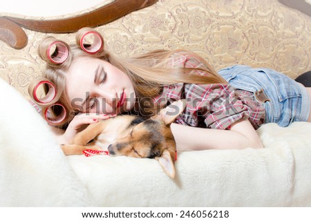 Sleeping cute dog and blond beautiful pinup girl with red lips curlers in her hair lying in bed