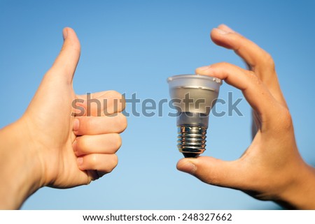 LED lamp in hand and thumb up against blue sky