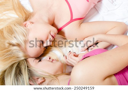 Close up portrait of 2 beautiful sisters or best girlfriends in pajamas having fun relaxing lying on white bed head to head