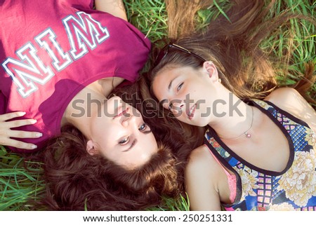 Close up on 2 beautiful young women girls friends having fun lying on grass happy smile on green outdoors background