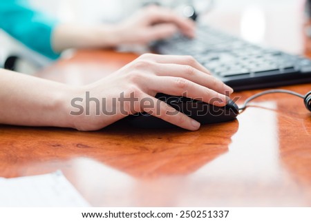 Close up on female hand holding computer mouse at office desk and typing on keyboard