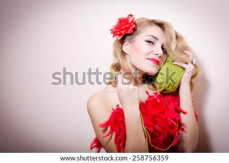 Glamour blond pinup girl in red dress with flower in her hair and green thread on light copy space
