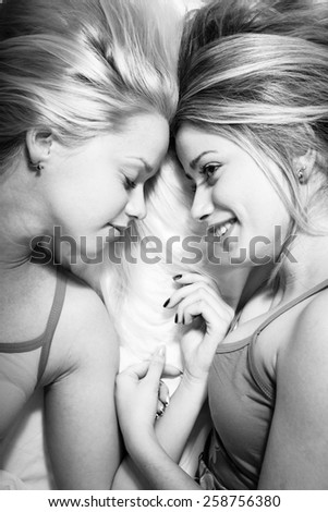 Black and white photo of two beautiful girls lying in bed head to head