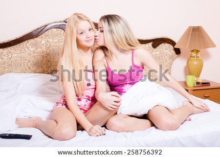 Portrait of two sexy beautiful young ladies having fun kissing and sitting in bed