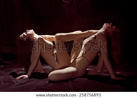 Two beautiful sexy women show play dancing performance and looking up at light on black stage background