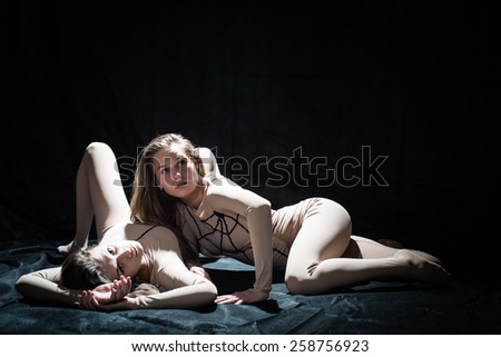 Two beautiful sexy women in performing bodysuits posing on black stage background