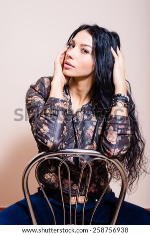 Portrait of beautiful brunette fashion girl with long hair sitting on chair and looking at camera