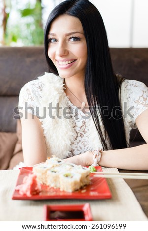 Portrait of young brunette pretty lady eating sushi in restaurant