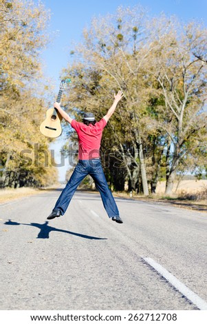 Man with guitar jumping in the middle of road