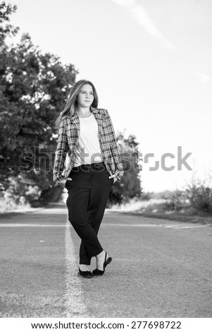 Portrait of happy young lady in formal wear standing on country road, black and white photography