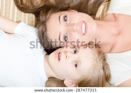 Closeup portrait of beautiful attractive mother and little daughter lying face to face on the sofa