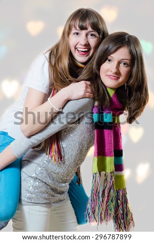 Young female riding on her sister\'s back having fun together on bokeh background with heart shaped spots