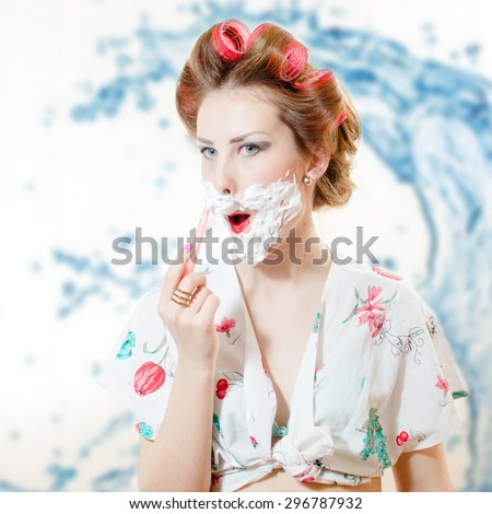 Beautiful young pinup woman shaving face with foam and razor looking in camera on bokeh background closeup portrait