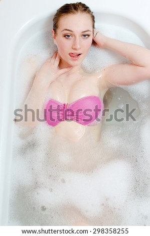 Young sexy blond woman pink swimsuit lying in foam bath