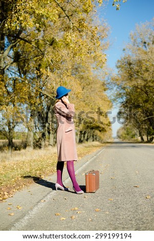 Lady in retro hat and overcoat with vintage suitcase hitchhiking