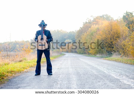 Man holding guitar with both hands on country road.