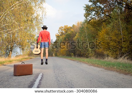Image of man in shorts hitchhiking on sunny fall day