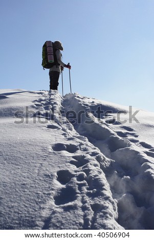 backpacker moving up in winter mountain under blue sky