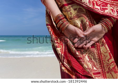 Close up of hands and bangles of a woman wearing a saree looking out to sea.
