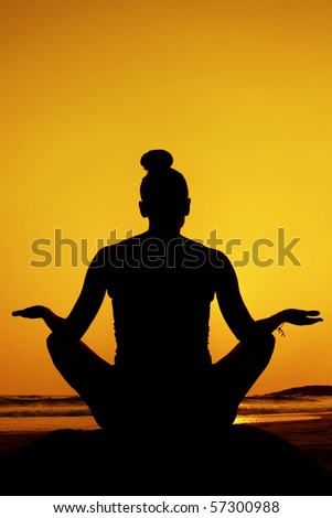 Silhouette of a woman doing yoga/meditation pose at sunset on the beach.