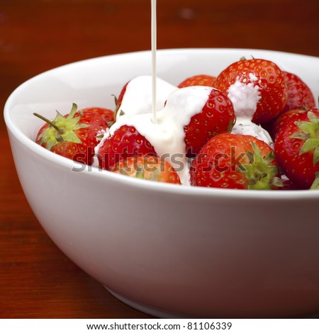 Cream being poured over a bowl of strawberries.