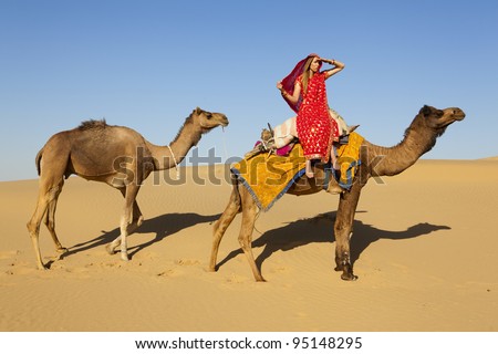 Young women wearing a saree riding a camel on the dunes of the Thar Desert, Rajasthan - India