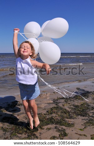 The cute little blonde girl in a white dresses with white balloons on the beach