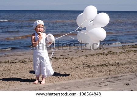 Cute little blonde girl in a white dresses eating the ice-cream on the beach