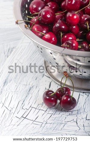 Metal colander filled with cherries over a rustic background