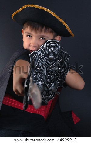 The boy in a suit of the pirate with a sword and a board on a black background