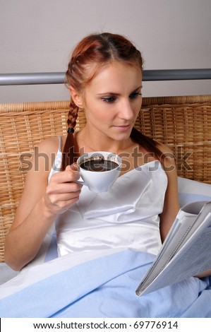 The young woman in bed at breakfast reads the newspaper