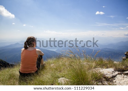 Woman sitting on mountain top of Monte Generoso admiring mountain landscape around Lugano lake and blue sky.